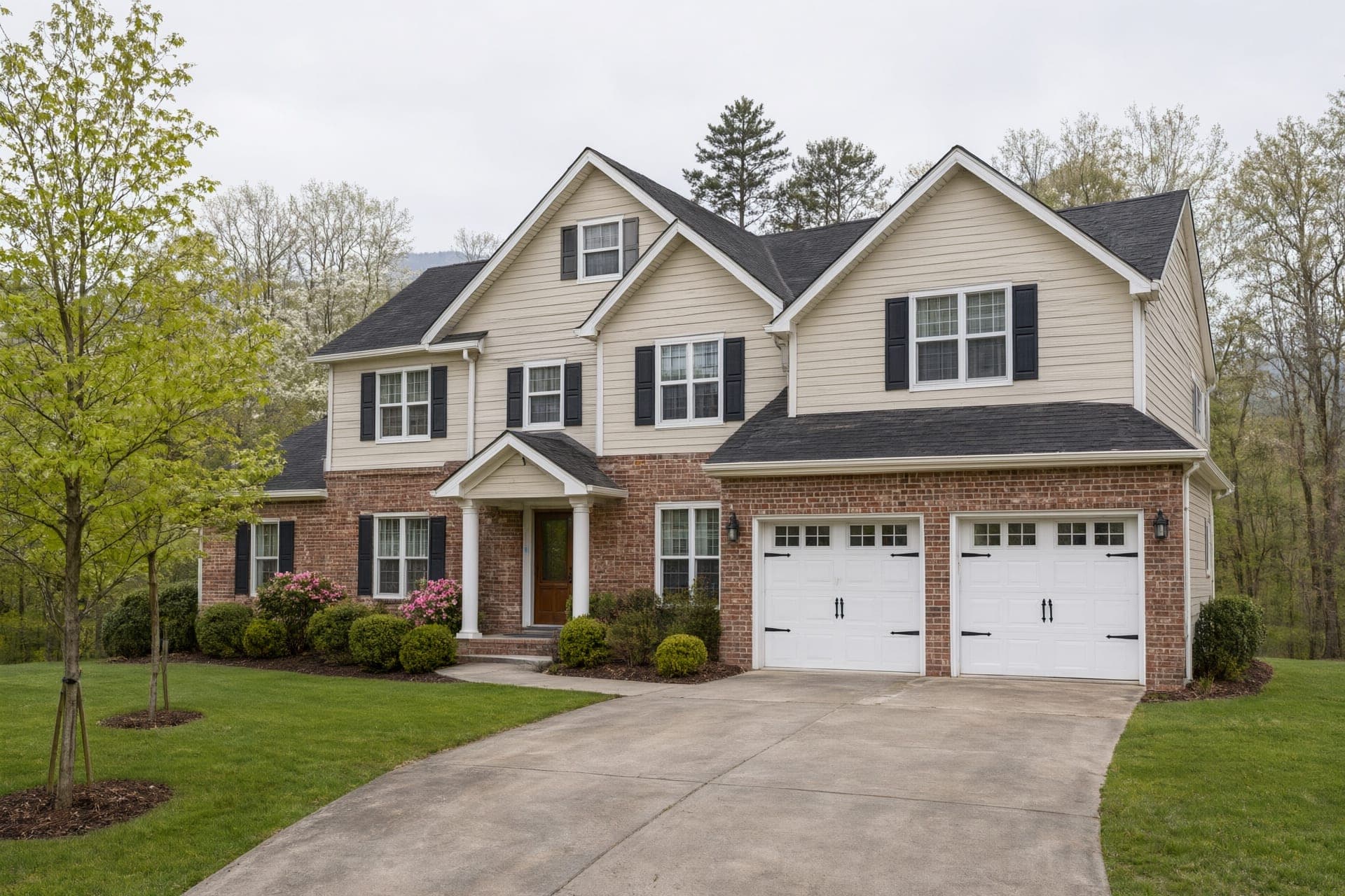 Large two-story house with a brick front, beige siding and a two-car garage on a spring lawn
