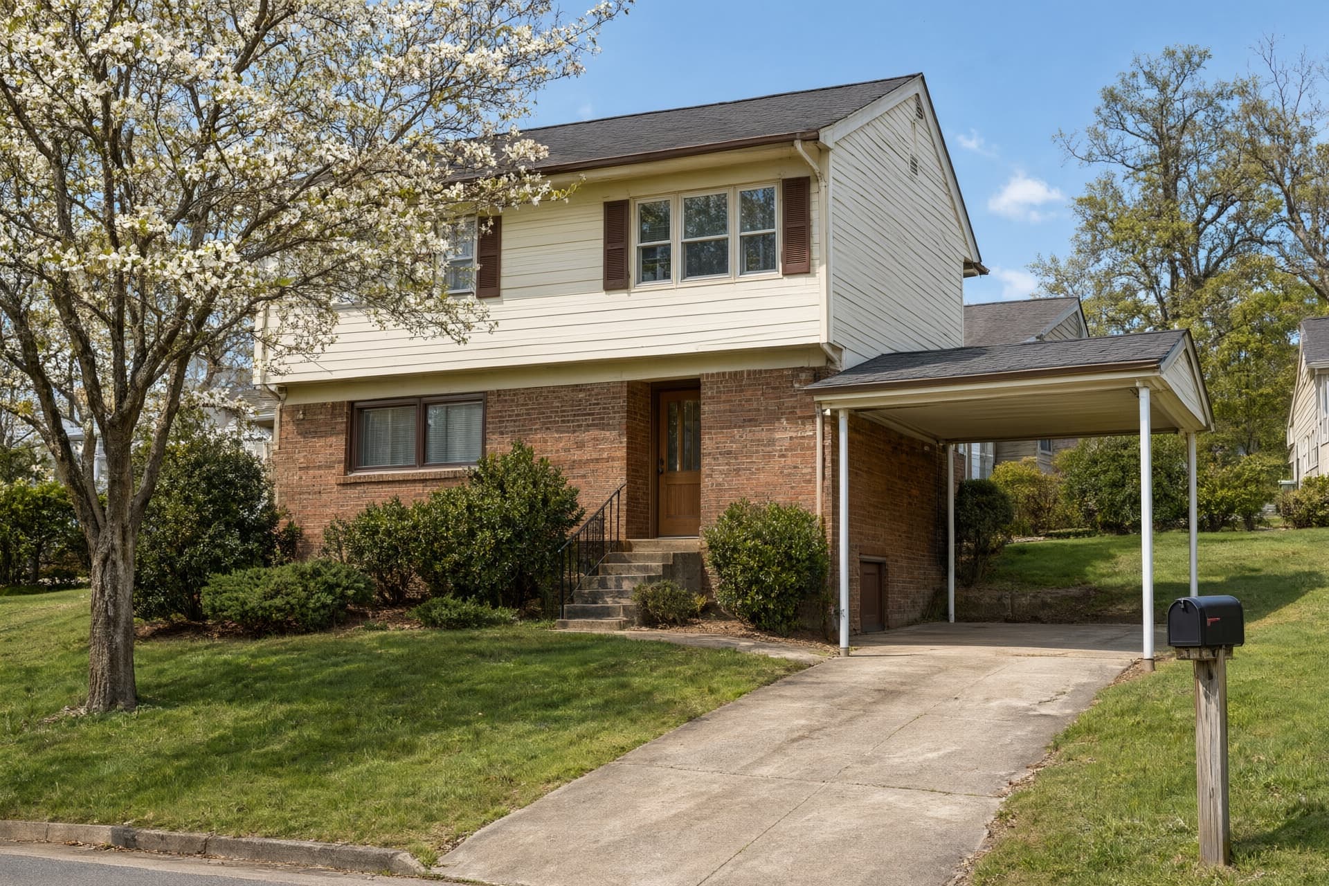 Split-level house with a brick lower level, light siding above and a carport on a sloped lawn